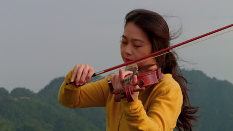 close-up of a long-haired woman gently playing the violin outdoors