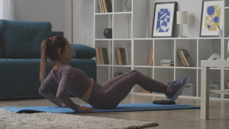 sporty woman is doing crunches on floor in living room of modern apartment training home at quarantine healthy lifestyle and sport activities