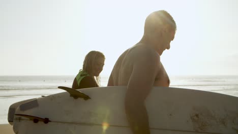 pareja sosteniendo tablas de surf y caminando por la playa