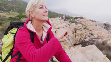 senior hiker woman with backpack with hand on her chin sitting on the rocks