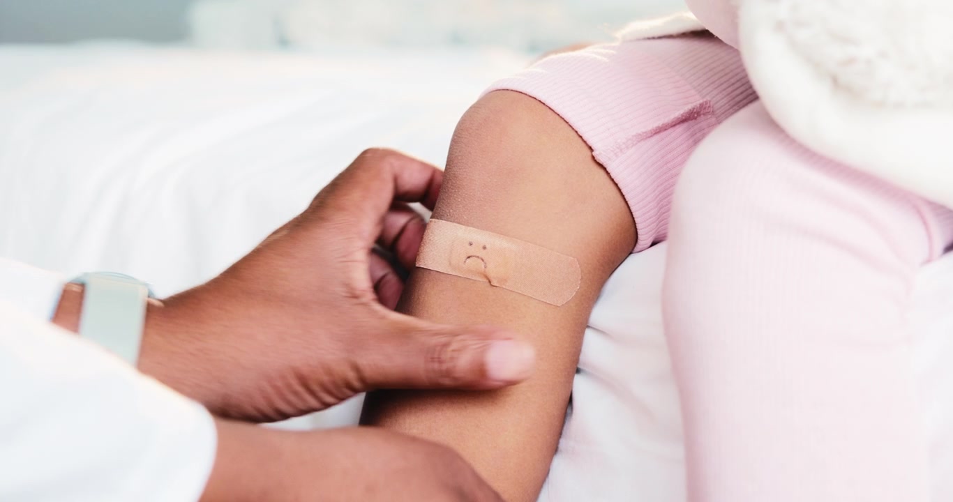 Medico che applica un cerotto adesivo sulla gamba di un bambino