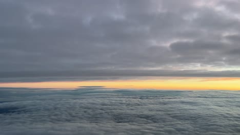 pilot view from a jet cockpit while flying between layers of clouds at dawn with an orange sky, at 10000m high in a cold winter moorning