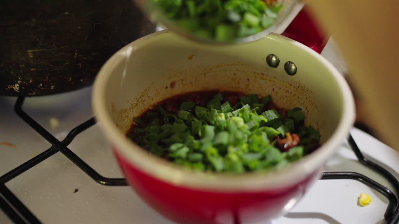 Fresh green onions being added to a spicy fried sauce for Locro in cooking pot.