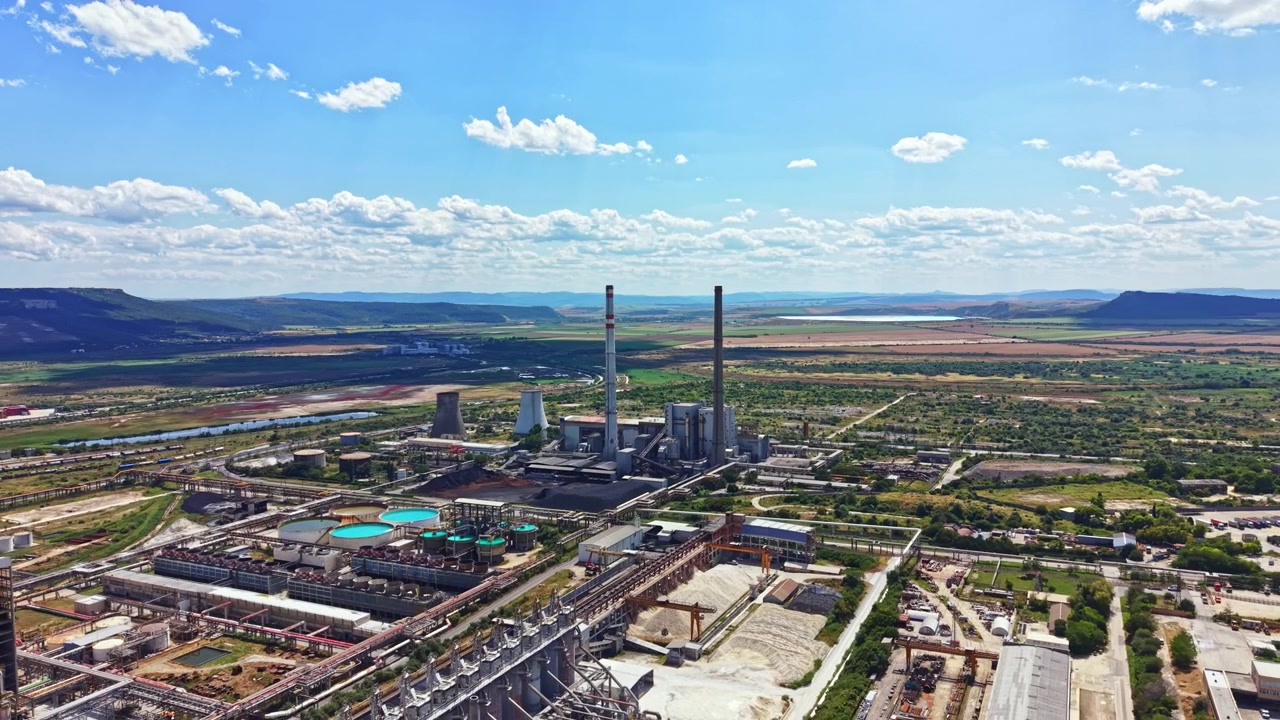 Área industrial com usinas de energia e montanhas ao fundo durante o dia com céu limpo