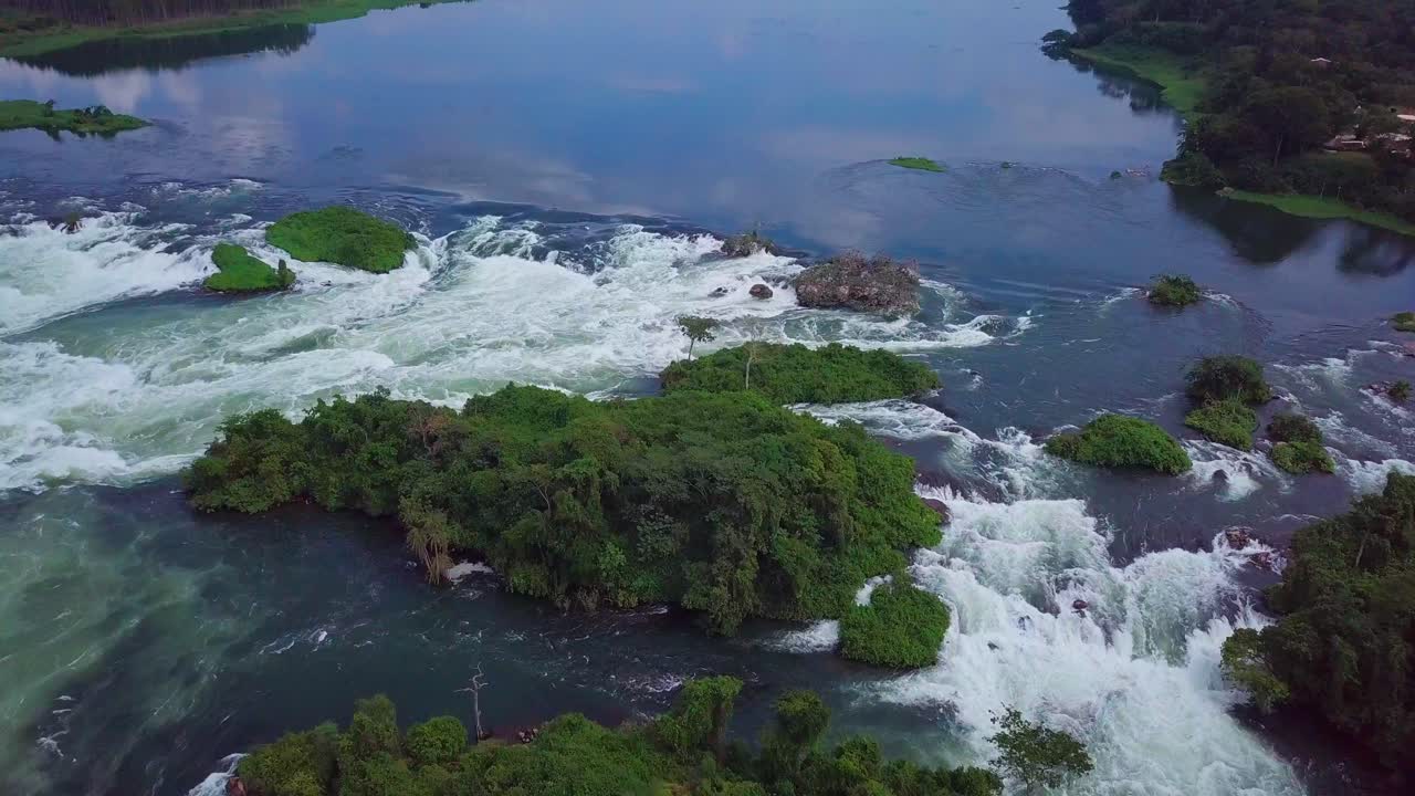 Aerial view of the source of the Nile River, with whitewater rapids flow through lush green islands and forests in Jinja, Uganda, a popular destination for whitewater rafting and kayaking, slow motion