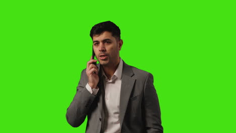 businessman wearing suit talking on mobile phone walking into frame against green screen background