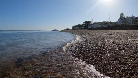 las olas de agua cristalina besan suavemente la playa de guijarros naranja en la isla de wight.
