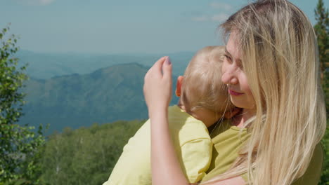 Happy-mother-strokes-little-son-against-distant-mountains