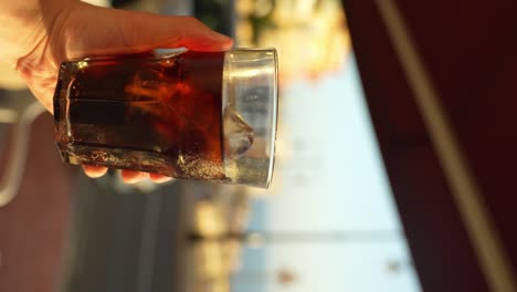 Person-holding-delicious-Cuba-libre-in-tropical-resort,-vertical-view