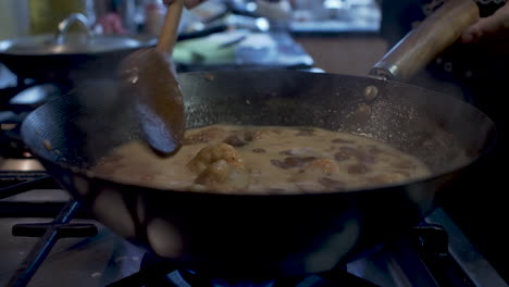 langostinos revueltos en salsa burbujeante a fuego lento dentro del wok con cuchara de madera