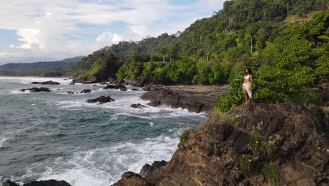 Young-woman-standing-on-edge-of-cliff-looking-out-over-the-ocean