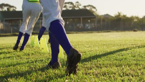 diverse group of female baseball players exercising on pitch, running between cones