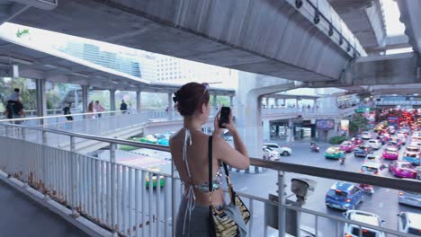 woman taking picture of city traffic from an overpass in bangkok, thailand