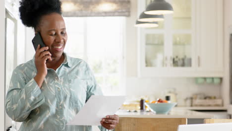 Mujer-Mayor-Afroamericana-Haciendo-Trámites-Y-Usando-Un-Teléfono-Inteligente-En-Una-Habitación-Soleada,-Cámara-Lenta