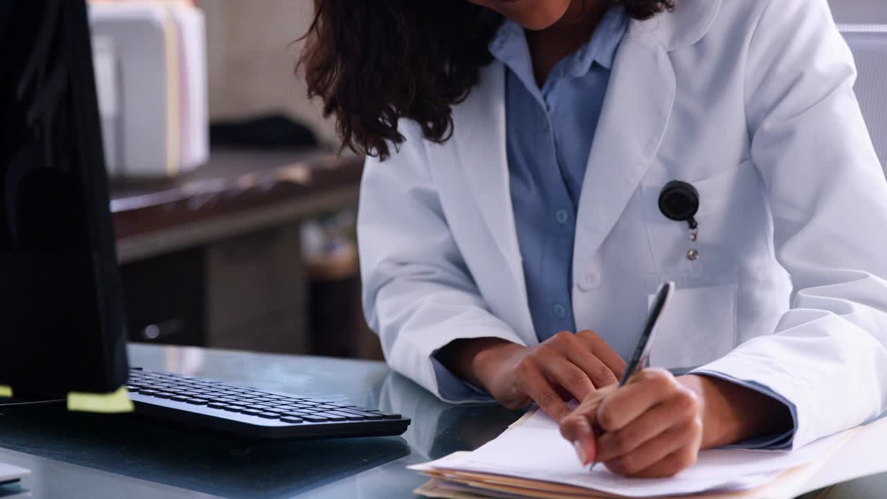 Young female doctor writes and uses computer at office desk