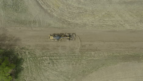 grader levels the surface on remote farm dirt road, overhead drone