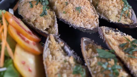 authentic freshly oven cooked mussels spinning on a black plate with sliced vegetables close up shot