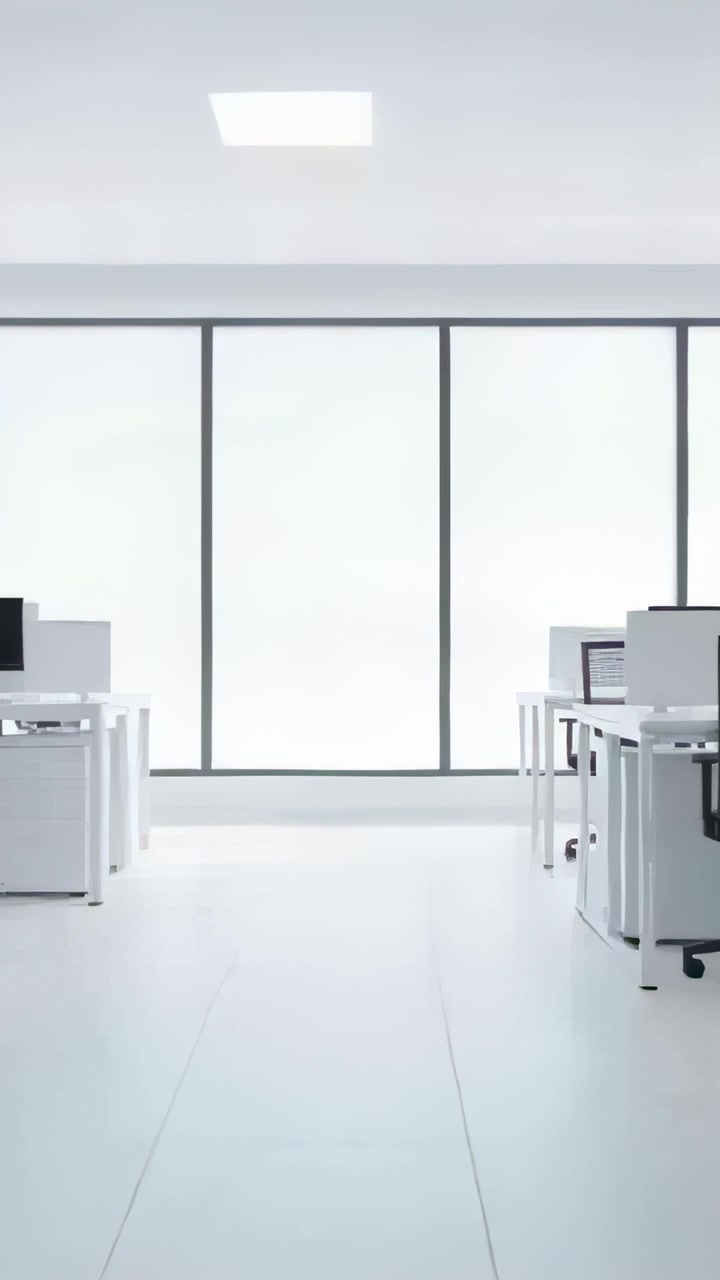 Vertical video: Panning camera showing empty aisle and desks at modern office with frosted windows