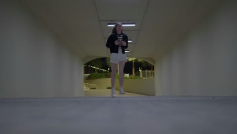 A-girl-with-medium-length-blonde-hair-runs-through-a-luminous-tunnel-in-a-skateboard-park-with-her-hair-waving-freely-as-she-runs----shot-at-a-low-angle