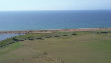 wide aerial tracking forward over a field at the west side of chesil beach, dorset