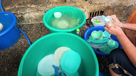 person scrubbing and rinsing dishes in buckets outside