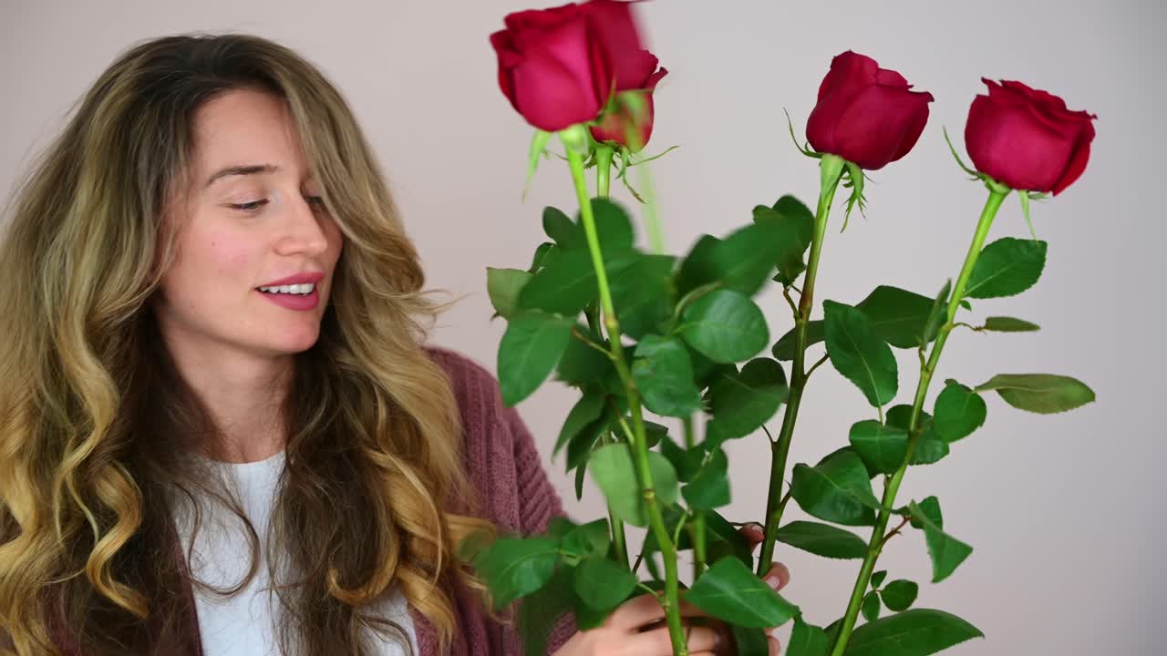 Beautiful blonde woman happily arranging red roses in a vase. Joyful Valentines day. Relationships and feelings concept. Front view