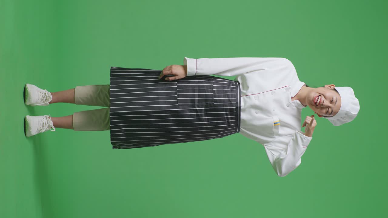 Full Body Of Asian Woman Chef Smiling And Making Call Me Gesture To Camera While Standing In The Green Screen Background Studio