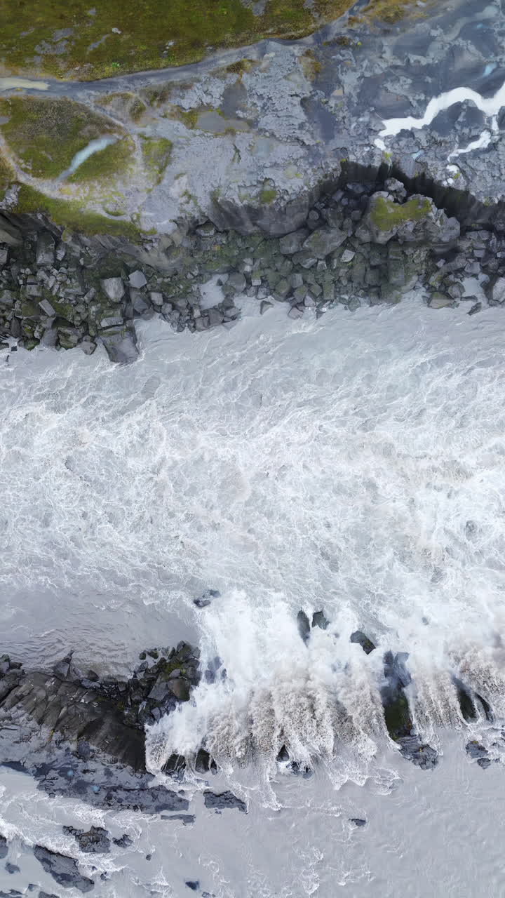 Veduta aerea con drone dell'immensa cortina d'acqua della cascata Dettifoss. Acque impetuose e turbolente si riversano dal ciglio della scogliera in un canyon avvolto dalla nebbia. Verticale.