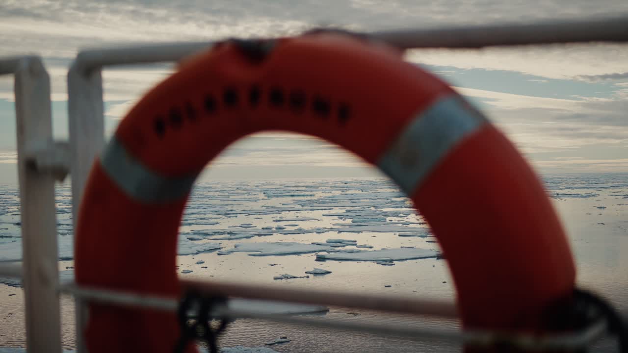 Arktisches Meereis, gerahmt durch eine verschwommene Rettungsboje am Geländer eines Expeditionsschiffes.