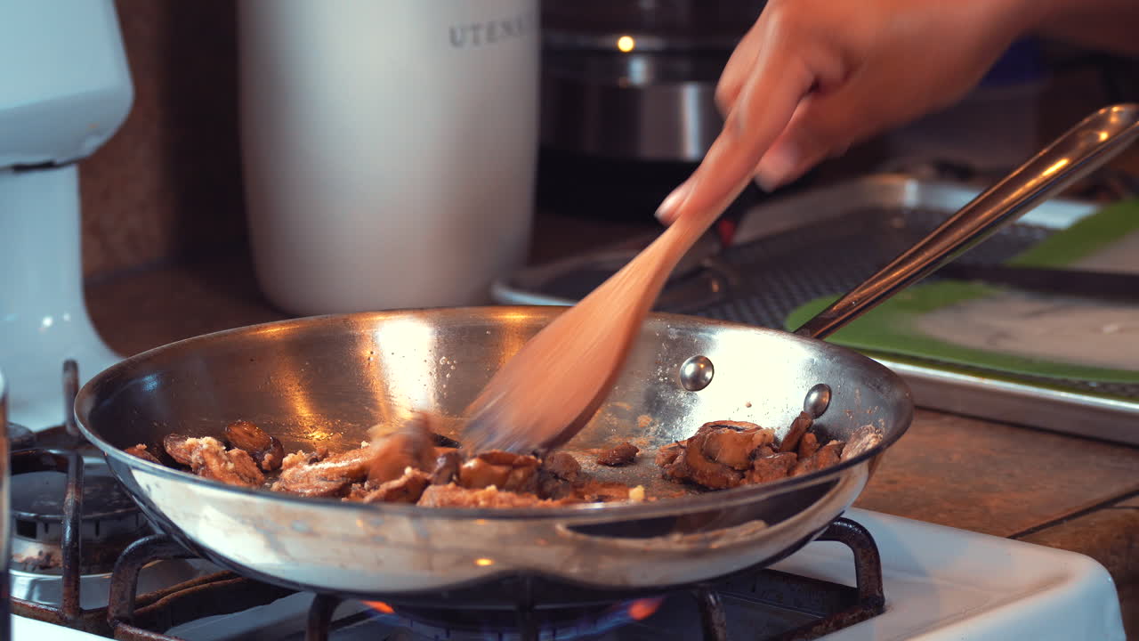 saltear y revolver los champiñones en una sartén sobre la llama de una estufa de gas