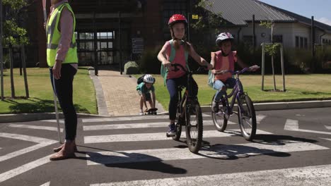 Dos-Niñas-Con-Mochilas-Escolares-Andando-En-Bicicleta-Y-Cruzando-La-Calle