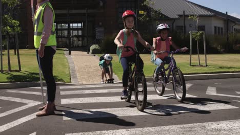 two girls with school bags riding bicycles and crossing the road