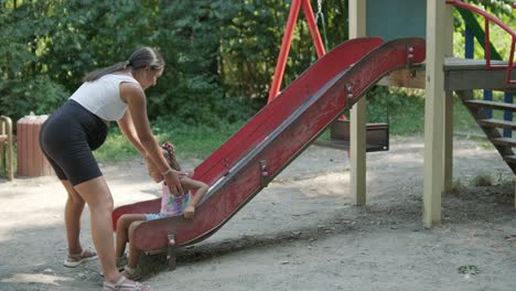 pregnant mother watching daughter play on slide at playground