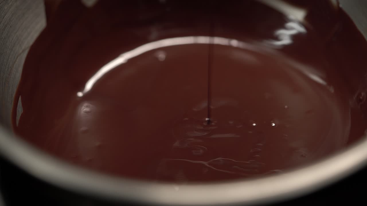 agitar manualmente el chocolate derretido en la olla usando una cuchara plana, disparo de 4k de cerca