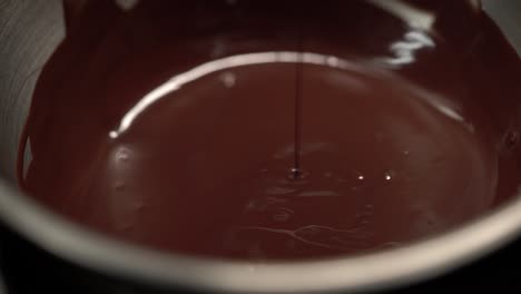 manual stirring melted chocolate in the pot using a flat spoon, close up 4k shot