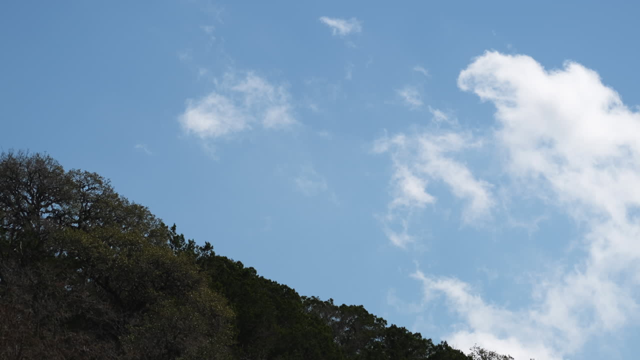 Whispy clouds slowly moving over the tree covered hill tops on a sunny day