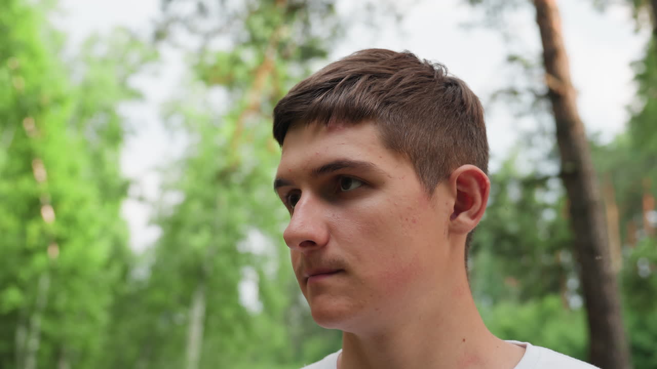 Medium view of young explorer standing in forest wiping sweat from face with palm under summer light, showing exhaustion, determination, and connection with nature during outdoor adventure