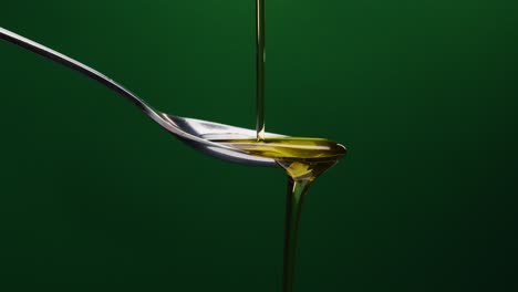 static shot of spoon over which oil is poured against green background