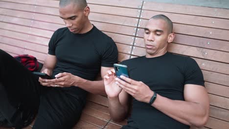 two relaxed bald african brothers typing on phones