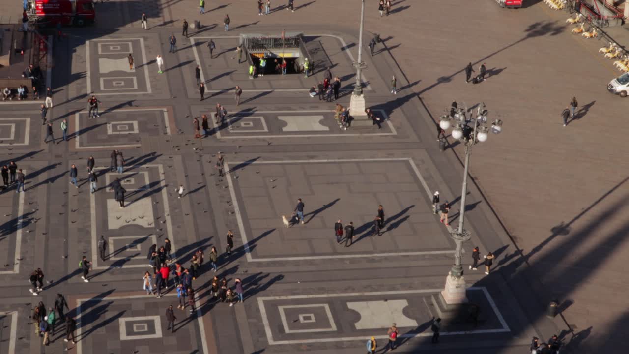 Duomo square seen from the church roof with people walking down and their shadows in the morning, panning medium wide shot