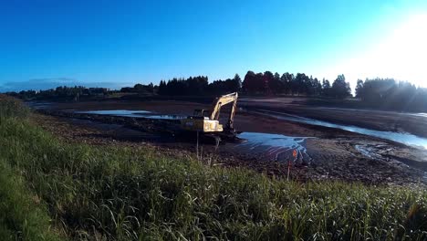 yellow excavator works with bucket to clear mud sludge and debris from the bottom of the drained river-3