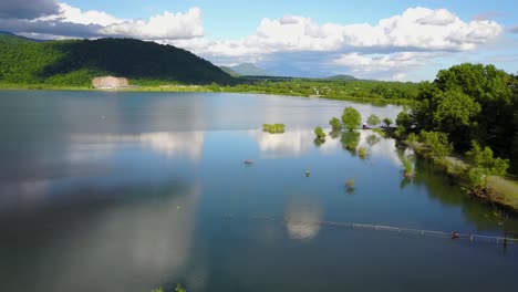 Fly-down-landing-drone-on-a-lake-in-spring-season-with-green-leaves-trees-around-the-nature-with-blue-sky-with-white-clouds-landscape-in-a-rural-area-in-azerbaijan-reclects-the-sky-in-water-beautiful