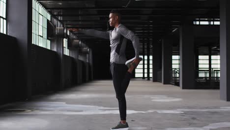 hombre afroamericano estirando las piernas en un edificio urbano vacío