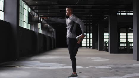 african american man stretching his legs in an empty urban building