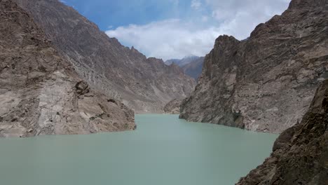 Aerial-over-a-glacier-fed-river-with-steep-rocky-cliffs-rising-to-tall-mountains