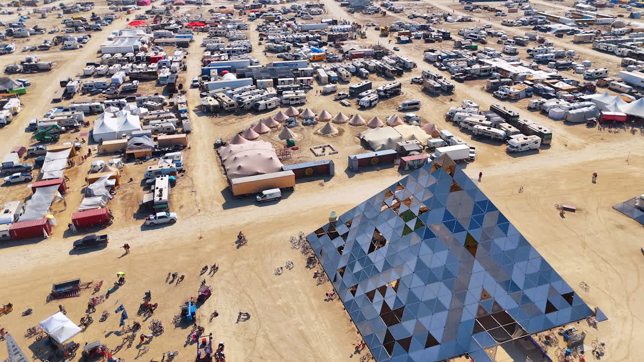 Approaching the pyramid art installation with mirror segments. The Burning Man festival. Campsite of the participants at backdrop