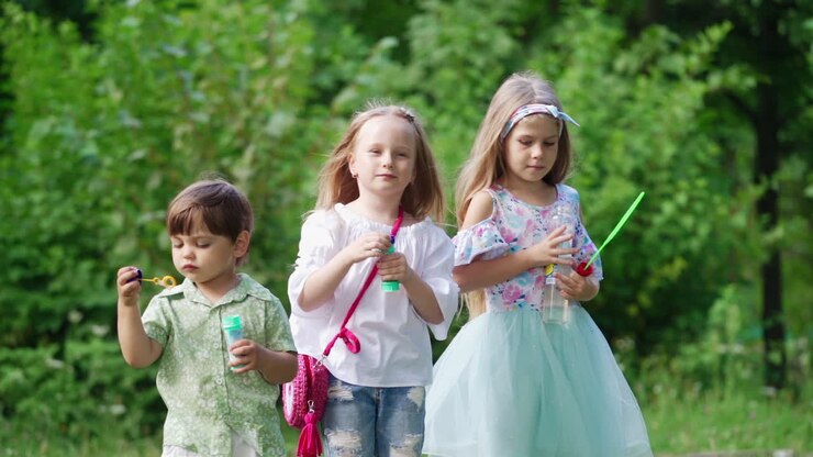Cute children spending good time in the park. Little girls and a boy blowing soap bubbles outdoors. Happy childhood in summer.