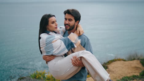 Happy-man-holding-woman-on-hands-walking-at-gloomy-sea-shore.-Romantic-couple