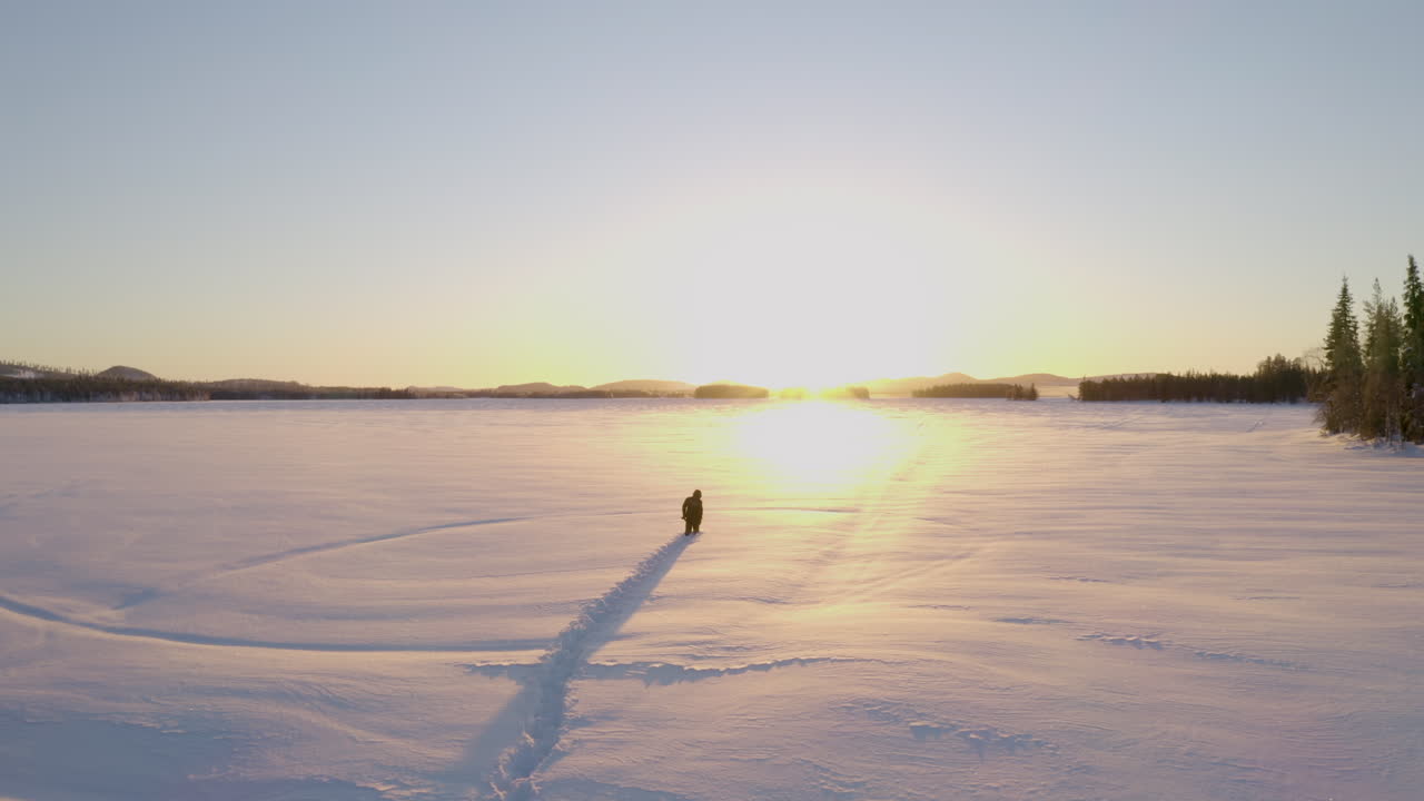 Following male walking in deep frozen ice lake snow towards glowing golden Swedish sunrise
