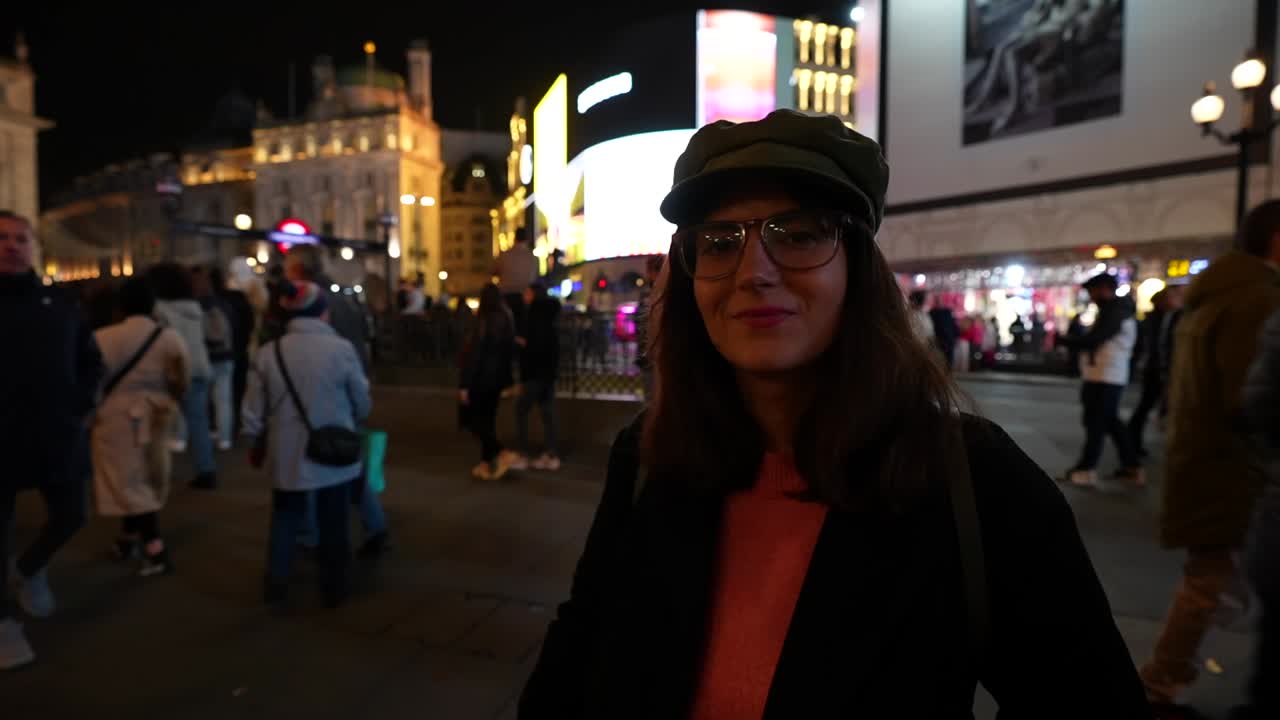 Woman smiling in Piccadilly Circus at night, surrounded by crowds and illuminated city lights. London